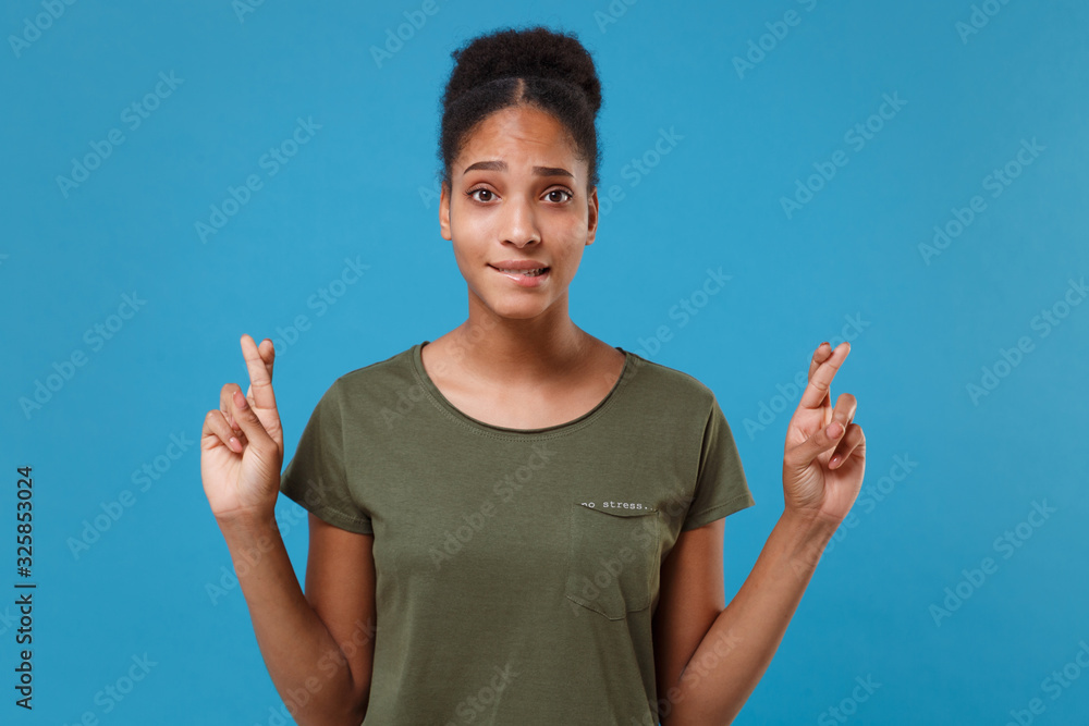Young african american woman girl in casual t-shirt posing isolated on blue background. People lifestyle concept. Mock up copy space. Waiting for special moment keeping fingers crossed, making wish. Young african american woman girl in casual t-shirt posing isolated on blue background. People lifestyle concept. Mock up copy space. Waiting for special moment keeping fingers crossed, making wish.
