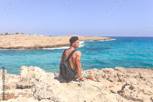 Athletic young man in cap sitting around Natural Rock Bridge at Cape Greco near Ayia Napa in the evening light. Cyprus. Healthy lifestyle