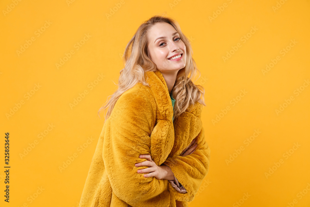 Smiling cheerful young blonde woman girl in yellow fur coat posing isolated on orange background in studio. People emotions lifestyle concept. Mock up copy space. Holding hands crossed looking camera. Smiling cheerful young blonde woman girl in yellow fur coat posing isolated on orange background in studio. People emotions lifestyle concept. Mock up copy space. Holding hands crossed looking camera.