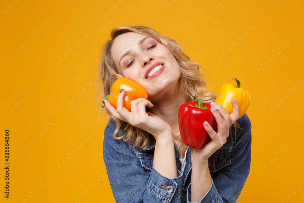 Smiling woman in denim clothes isolated on orange background. Proper nutrition vegetarian food healthy lifestyle diet meal. Diabetes dieting concept. Hold colorful bell peppers keeping eyes closed. Smiling woman in denim clothes isolated on orange background. Proper nutrition vegetarian food healthy lifestyle diet meal. Diabetes dieting concept. Hold colorful bell peppers keeping eyes closed.