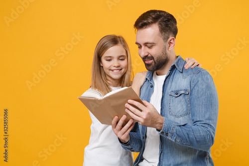 Pretty bearded man in casual clothes have fun with cute child baby girl. Father little kid daughter isolated on yellow background in studio. Love family day parenthood childhood concept. Reading book.