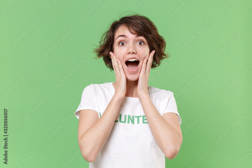 Surprised young brunette woman in white volunteer t-shirt isolated on pastel green background studio portrait. Voluntary free work assistance help charity grace teamwork concept. Put hands on cheeks. Surprised young brunette woman in white volunteer t-shirt isolated on pastel green background studio portrait. Voluntary free work assistance help charity grace teamwork concept. Put hands on cheeks.