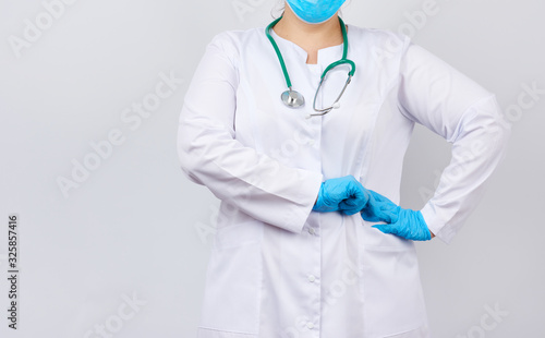 medic woman in white coat and mask, wearing blue medical latex gloves on her hands