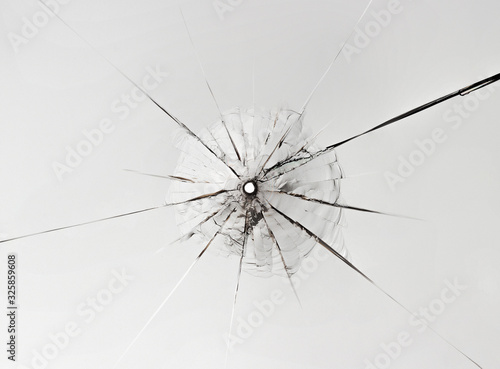 Small hole in glass with long cracks on white background.