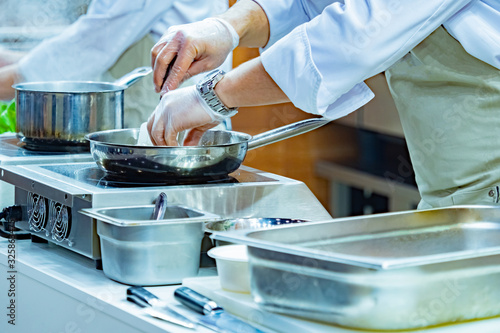 Chef's hands and frying pan close-up. The cook fries the food in the pan. Preparation of second courses. Restaurant kitchen. Cookware and appliances for the cafe. Stainless steel cookware.