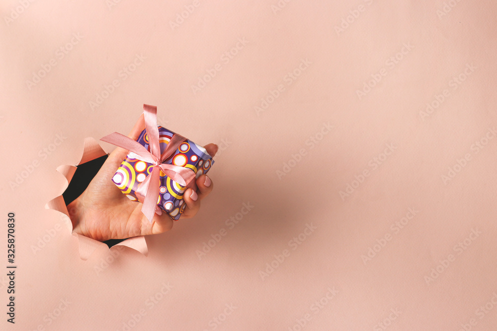 Female hand holding gift box through round hole in pink paper, Boxing day, Gift Expense Planning, Copy space