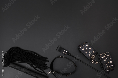 Leather handcuffs, black whip, collar and stack on black background photo