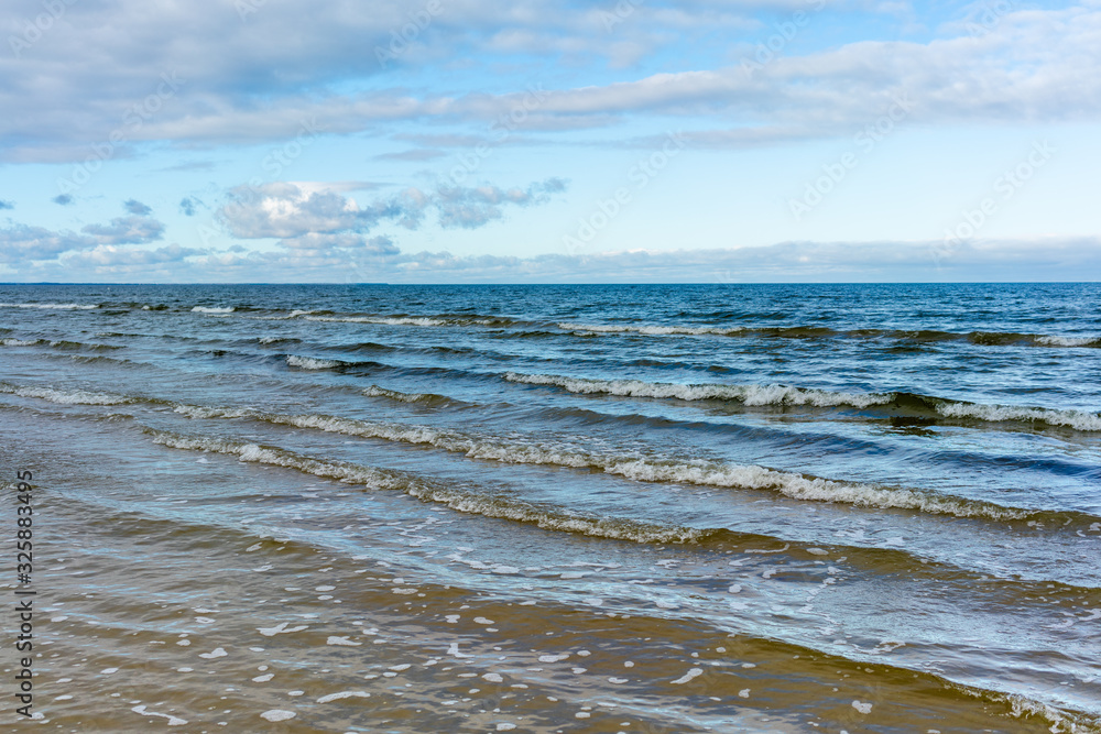 Beautiful view of the sandy shore of the Baltic Sea with waves and the sky with clouds.