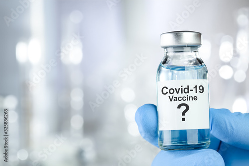 Possible cure concept with a hand in blue medical gloves holding Coronavirus, Covid 19 virus, vaccine vial