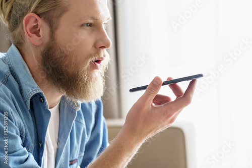 Foto Young man hold phone speak on speakerphone using virtual digital voice recognition assistant search on smartphone at home record audio message, mobile app ai tech concept, close up side view