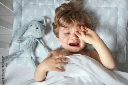 Baby crying in the bed before a bedtime. Child want to sleep. Toddler emotion before a sleeping. View from above.