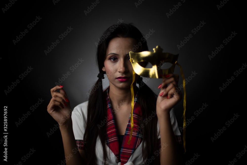Portrait of an Asian/Japanese/Korean brunette young girl in sexy school uniform with golden mask in a black/grey studio background. Fashion and cosplay photography. Portrait of an Asian/Japanese/Korean brunette young girl in sexy school uniform with golden mask in a black/grey studio background. Fashion and cosplay photography.