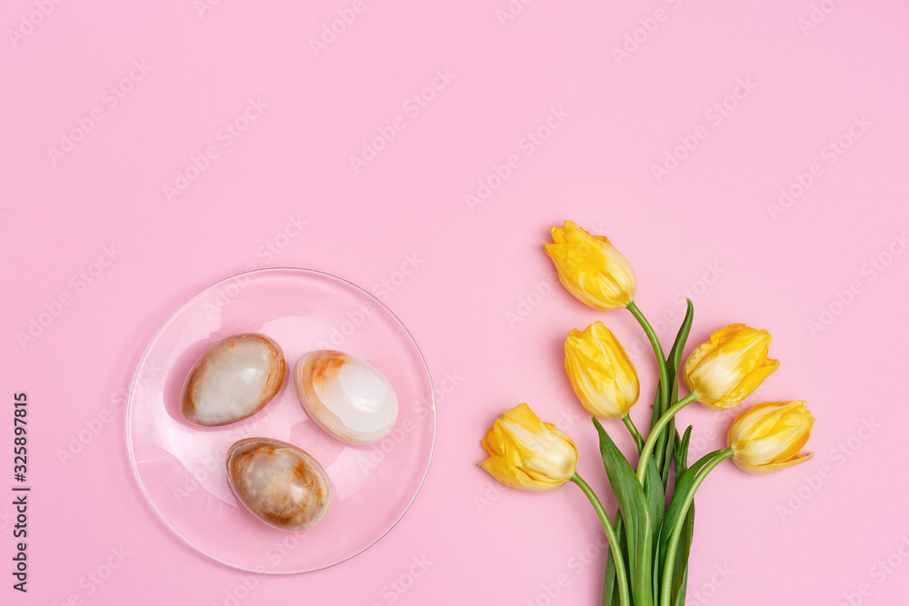 Stone Easter eggs and bouquet of beautiful yellow tulips. Minimal style composition with Easter concept. Spring blossom flowers. Top view and copy space.