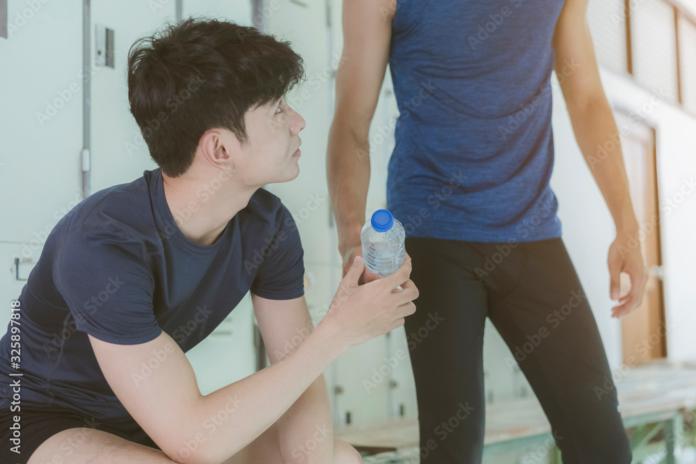 Young Asian man hand Pick up or giving bottle of fresh water to friend on locker room after fitness or exercise. lifestyle or relax and Refreshing Concept Young Asian man hand Pick up or giving bottle of fresh water to friend on locker room after fitness or exercise. lifestyle or relax and Refreshing Concept