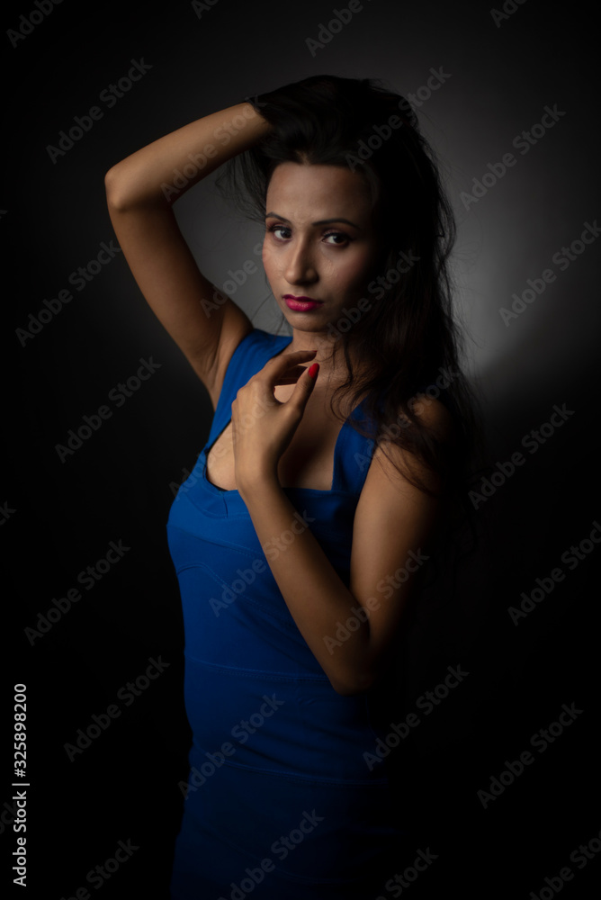 Fashion portrait of an young and attractive Indian Bengali brunette girl with blue western dress in front of a black studio background. Indian fashion portrait and lifestyle. Fashion portrait of an young and attractive Indian Bengali brunette girl with blue western dress in front of a black studio background. Indian fashion portrait and lifestyle.