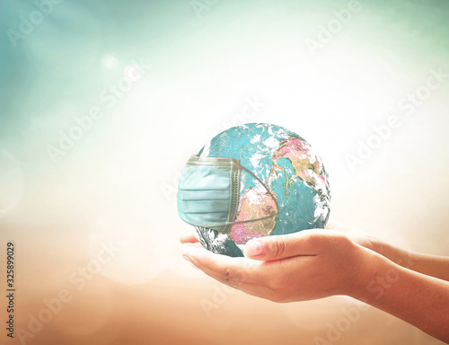 COVID-19 prevention concept: Human hands holding earth globe with medical disposable face mask. Elements of this image furnished by NASA photo