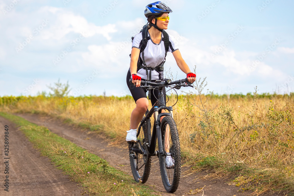 Obraz premium Beautiful girl cyclist rides on the field on a bicycle. Healthy lifestyle and sport. Leisure and hobbies