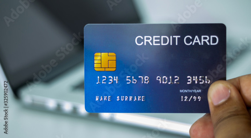 Close up holding a blue credit card placed in front of the laptop. online shopping payment and retail concepts. mockup and fake credit card