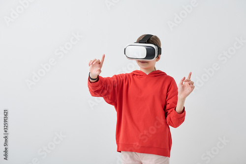 Content school girl in red hoodie gesturing hand while enjoying virtual reality in VR simulator