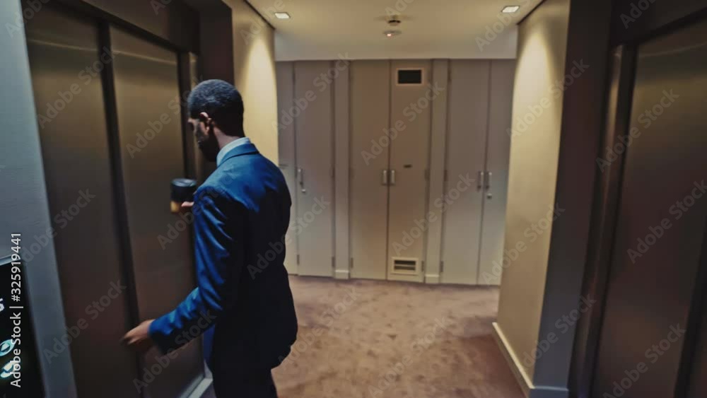 Tracking shot of a confident black businessman in an impeccably tailored suit walking into the elevator. Tracking shot of a confident black businessman in an impeccably tailored suit walking into the elevator.
