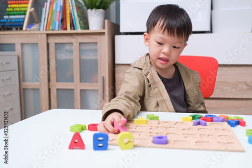 Cute smiling kindergarten boy playing with alphabet blocks, Asian children learning English with wooden educational abc toy puzzle for kids, Teach young kids English at home concept photo