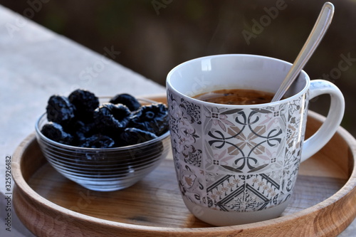 Porcelain cup with coffee served on the round wooden tray with blue dry plumes in small bowl. Closeup, selective focus.