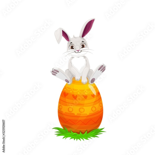 Easter bunny sitting on painted egg, Easter religious holiday and egghunting party. Vector white rabbit or hare animal with cute ears on spring green grass with orange egg and yellow pattern