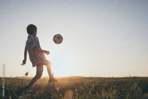 Young little boy playing in the field  with soccer ball.