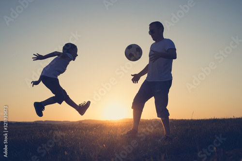 Father and young little boy playing in the field with soccer ball.