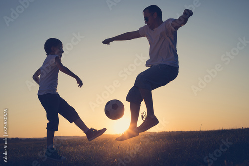 Father and young little boy playing in the field with soccer ball.