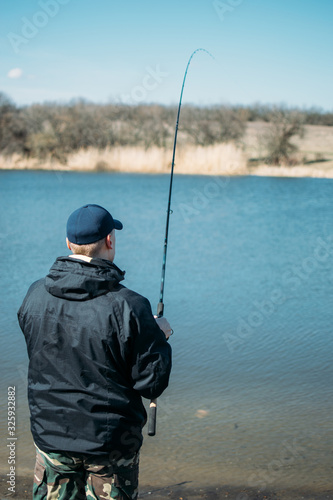 Feeder fishing. Male fisherman fishing at sun day on the lake. Man in jacket catches bream fish in early spring. Fishing hobby vacation concept