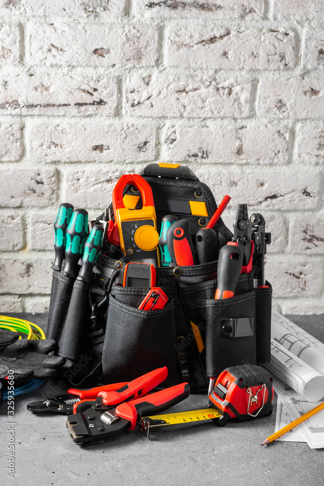 Electrician's tools in a black construction bag on a gray table against a white brick wall. Construction tools of an installer or electrician. Space for text