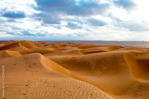 Wahiba Sand desert landscape of Sultanate of Oman - Curvy sand dunes pattern at sunset with cloudy sky.