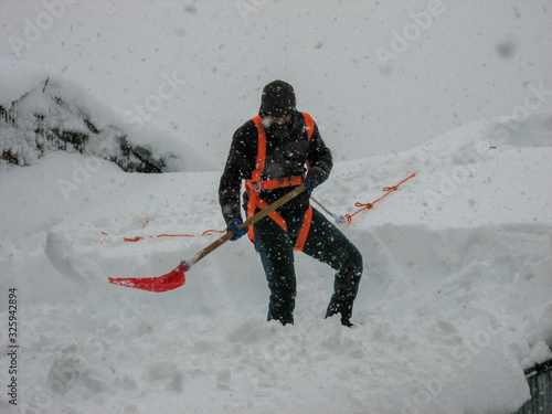 Rasht, Iran - February 11,2020: A man removes heavy snow from the roof of a house. Dangerous weight on a roof.