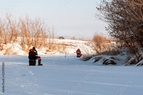 Fishermen catch fish on the ice of the river on a winter day.