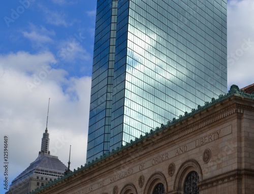 Closeup of glass skyscraper with blue cloudy sky reflected in it and older style stone building in foreground
