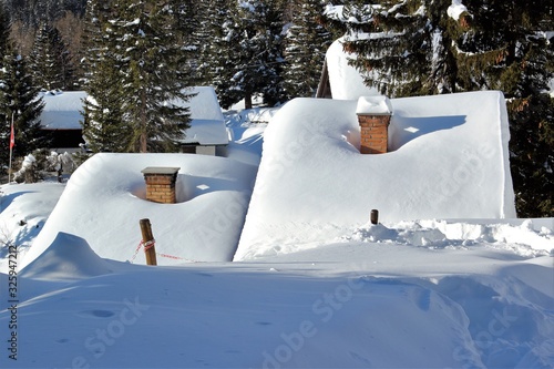 Casette sommerse nella neve a Carì, Svizzera Italiana con camini e pini ricoperti di neve photo