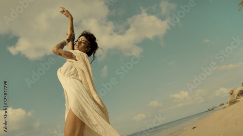 Seductive oriental woman at hot day under sun by the sea coast, walking and sensually posing