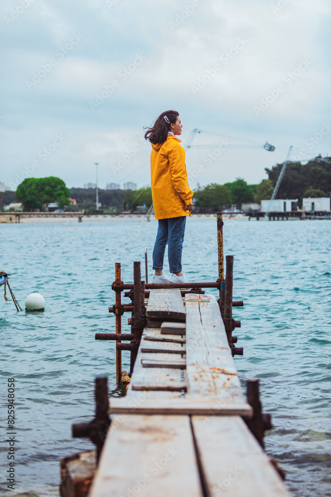 woman in yellow raincoat at sea pier looking at storming water