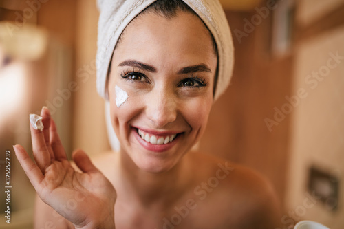 Young happy woman applying moisturizer on her face in the bathroom. photo