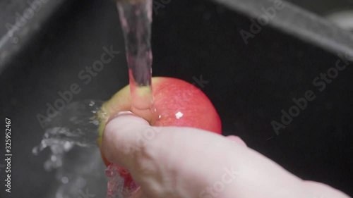 Slow motion view of man's hands washing carefully apple under running water. Avoiding getting infections of e. coli photo