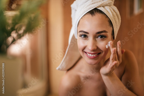 Beautiful woman applying moisturizer on her face in the bathroom. photo