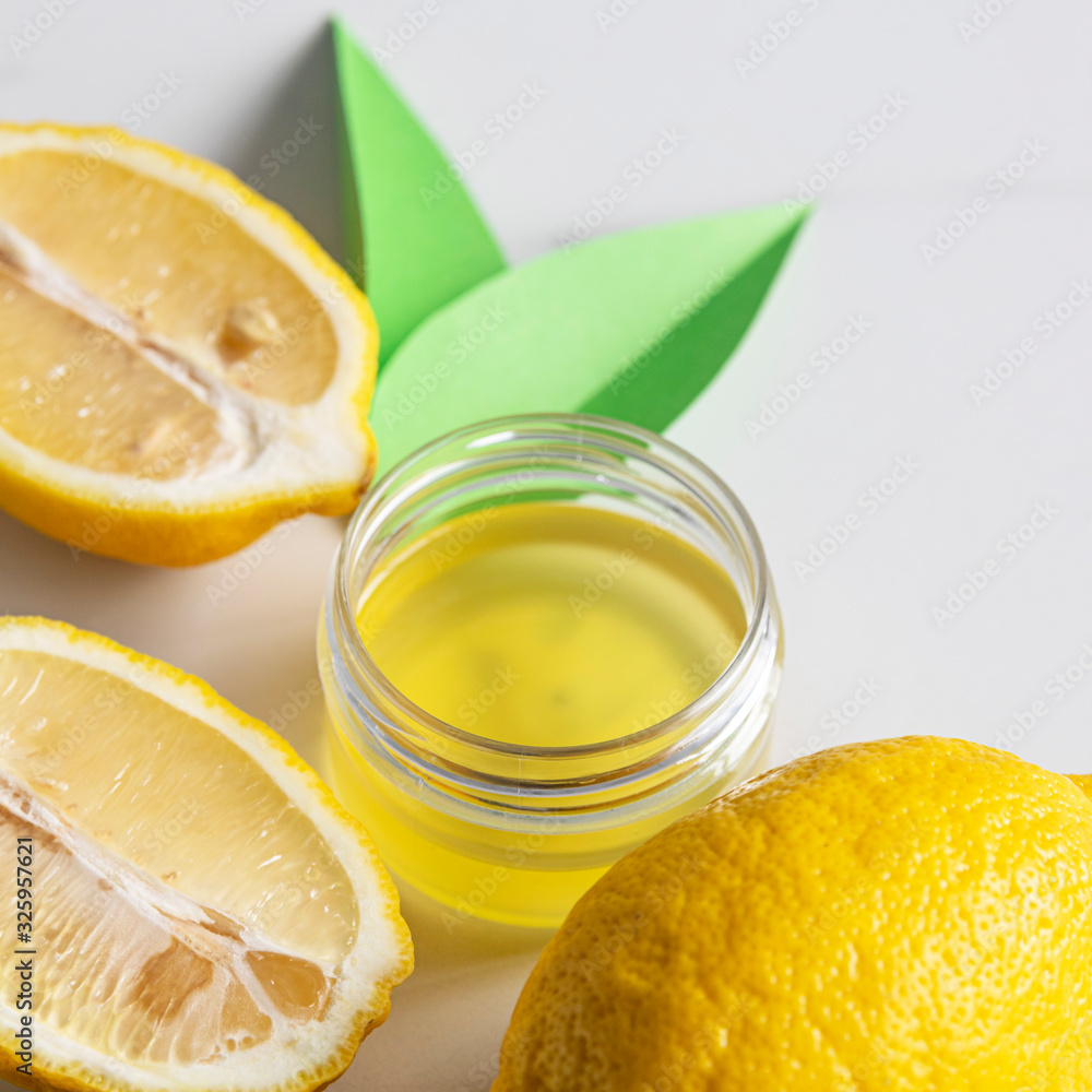 Yellow cosmetic liquid in glass jar and fresh lemon on marble background. Natural organic cosmetics concept. Homemade beauty product for body or face skin care Yellow cosmetic liquid in glass jar and fresh lemon on marble background. Natural organic cosmetics concept. Homemade beauty product for body or face skin care