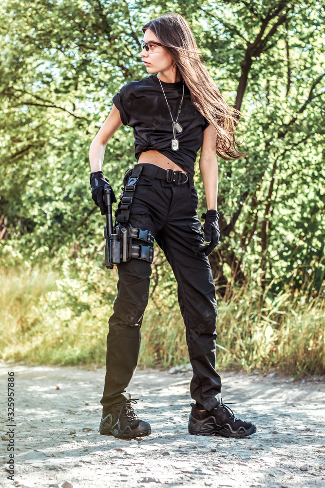 Girl in tactical clothes with a gun. Military woman. Black T-shirt and  pants. Holster.SWAT Stock Photo
