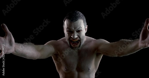 mad man is covered by white greasepaint is screaming standing in dark room, stretching hands photo