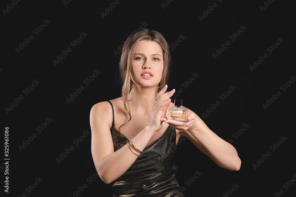 Naklejka premium Beautiful young woman with bottle of perfume on dark background