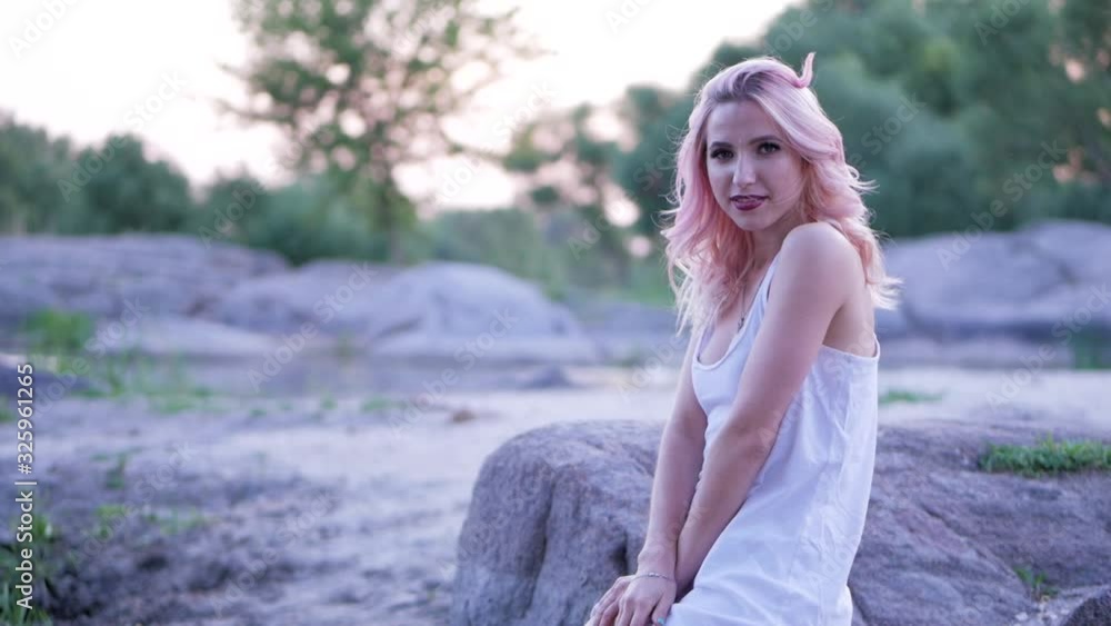 Beautiful blonde girl posing for the camera in a white t-shirt sitting on a rock Beautiful blonde girl posing for the camera in a white t-shirt sitting on a rock