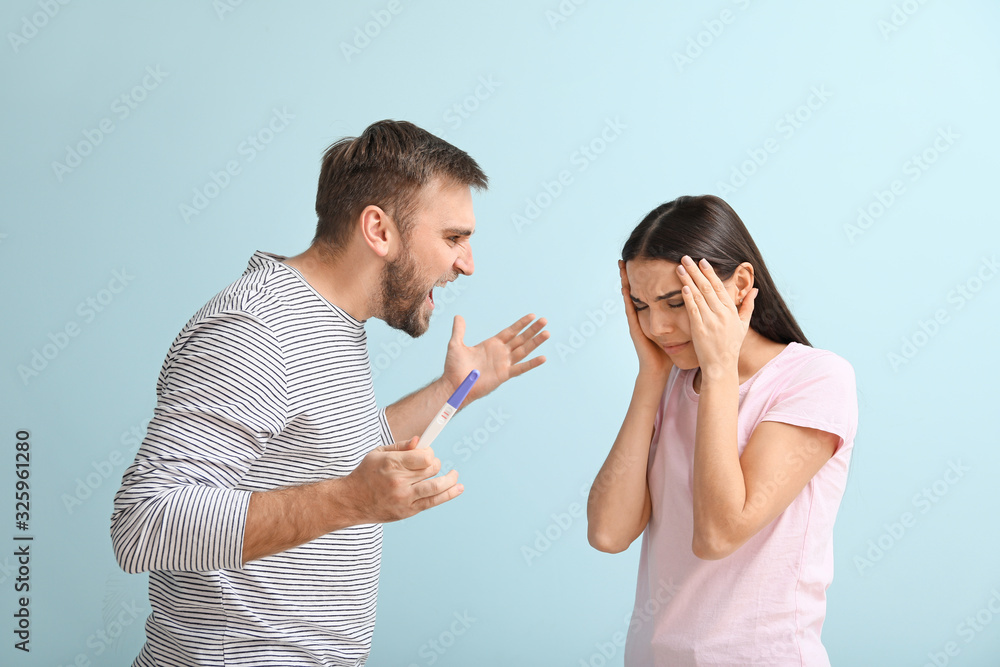 Emotional young couple with pregnancy test on color background Emotional young couple with pregnancy test on color background