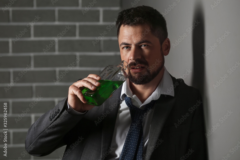 Businessman with absinth near grey wall. Concept of alcoholism Businessman with absinth near grey wall. Concept of alcoholism