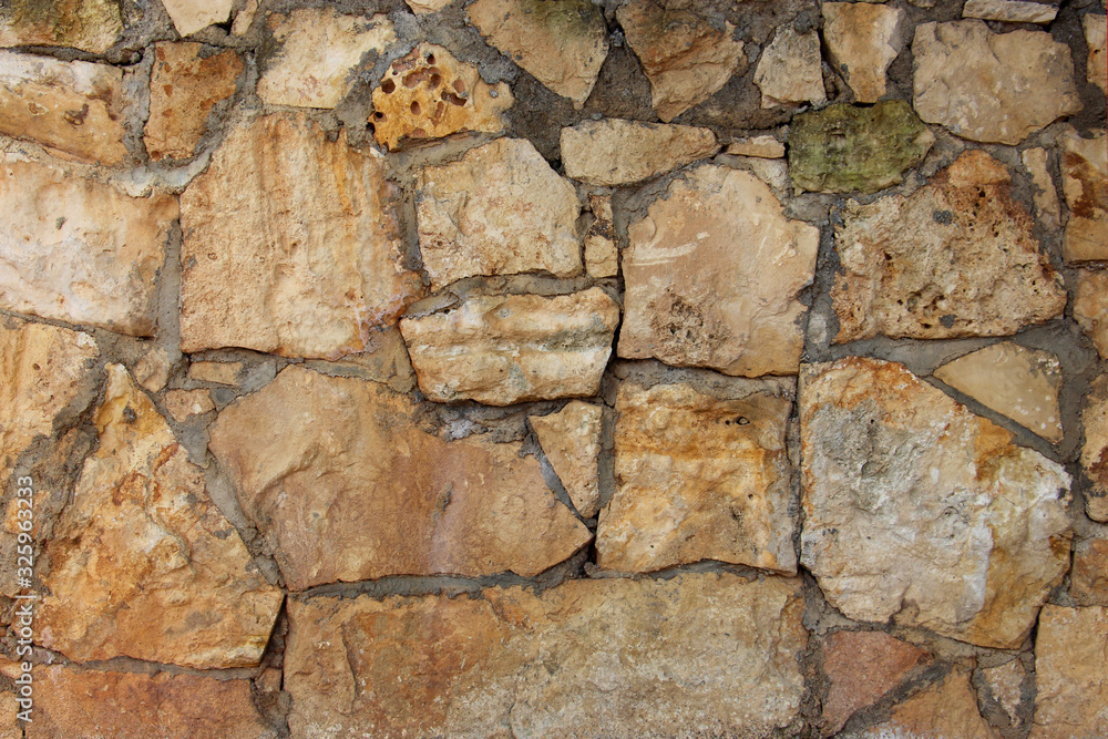 background of a solid stone wall of cement, limestone, sand and light multi-colored cobblestones with an uneven surface, of different sizes and shapes background of a solid stone wall of cement, limestone, sand and light multi-colored cobblestones with an uneven surface, of different sizes and shapes